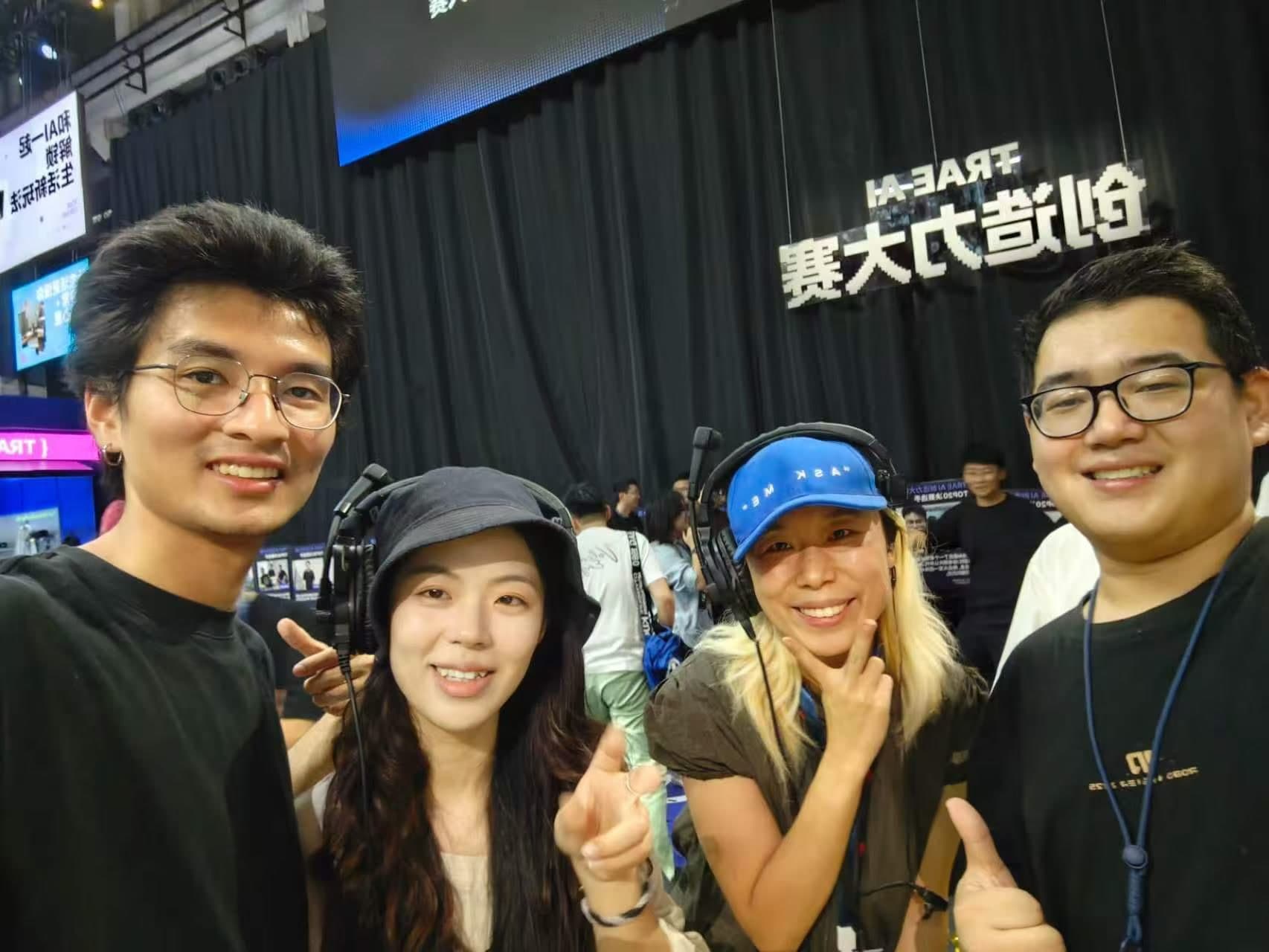 TRAE 创造力大赛背景前的四人合影，两位朋友戴着工作耳机